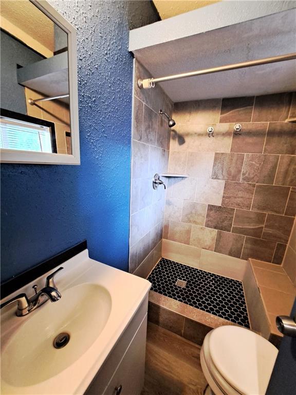 3009 Montgall Ave, Kansas City, MO 64128 - bathroom featuring tiled shower, vanity, a textured wall, and wood finished floors