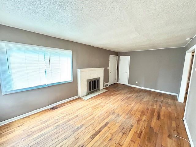 5046 Glenside Ct, Kansas City, MO 64129 - unfurnished living room featuring hardwood / wood-style flooring, a textured ceiling, and a brick fireplace