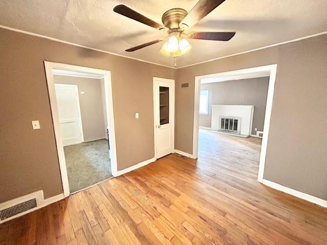 5046 Glenside Ct, Kansas City, MO 64129 - empty room with light wood-style flooring, a ceiling fan, and a glass covered fireplace