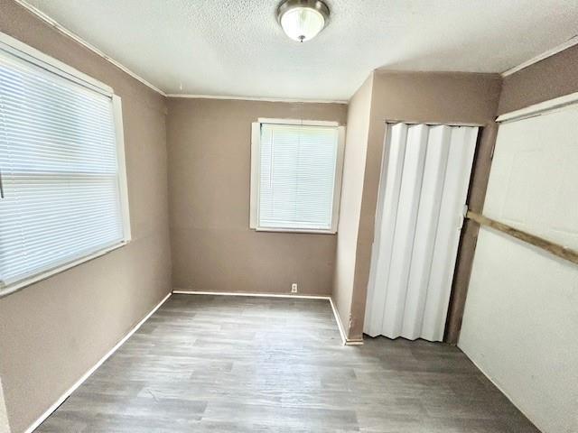 5046 Glenside Ct, Kansas City, MO 64129 - unfurnished bedroom with multiple windows, wood finished floors, a textured ceiling, crown molding, and a closet