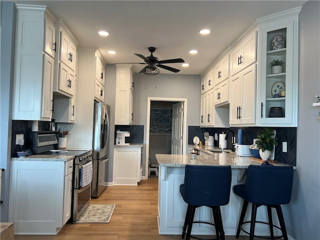 11681 S Roundtree St, Olathe, KS 66061 - kitchen featuring stainless steel appliances, a peninsula, a kitchen breakfast bar, a ceiling fan, and glass insert cabinets