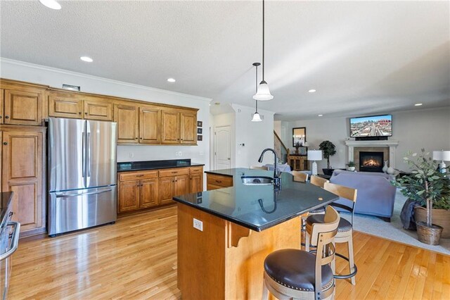 2712 SW Carlton Dr, Lees Summit, MO 64082 - kitchen featuring freestanding refrigerator, brown cabinets, light wood-style flooring, a glass covered fireplace, and a center island with sink