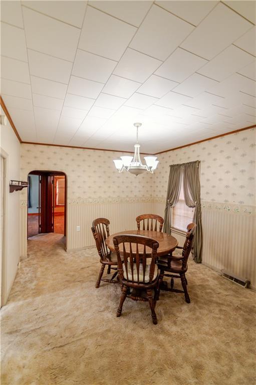 1134 Atchison St, Atchison, KS 66002 - dining room with wallpapered walls, light colored carpet, arched walkways, crown molding, and a chandelier