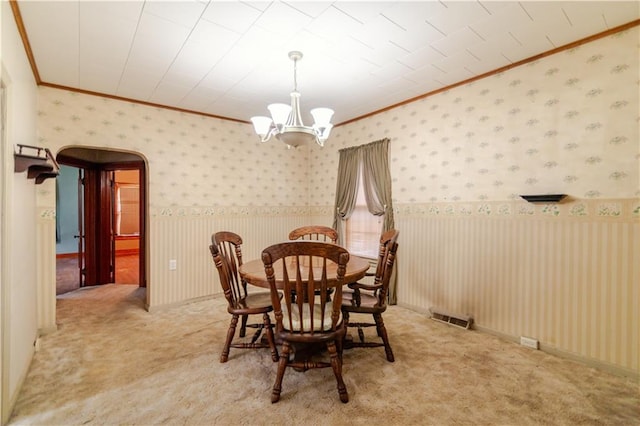 1134 Atchison St, Atchison, KS 66002 - dining space featuring a chandelier, ornamental molding, wallpapered walls, light carpet, and arched walkways