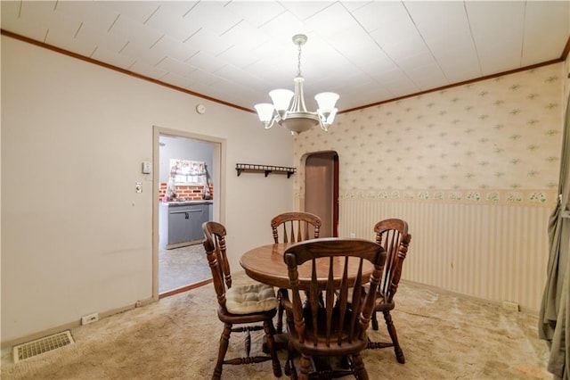 1134 Atchison St, Atchison, KS 66002 - carpeted dining room with crown molding, a chandelier, wallpapered walls, and arched walkways