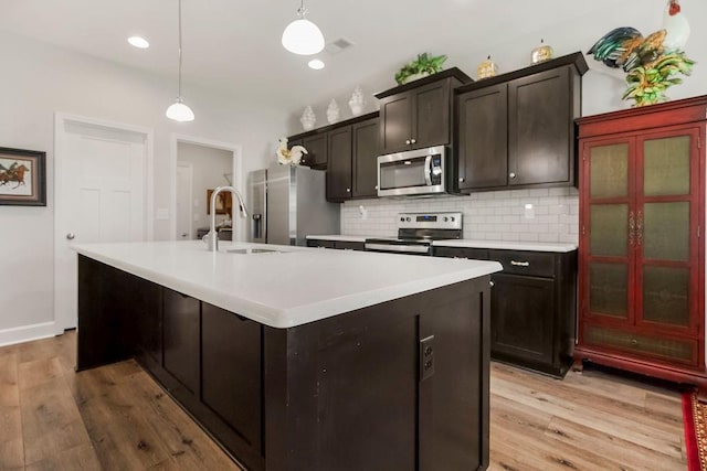 2214 SW 9th St, Blue Springs, MO 64014 - kitchen with appliances with stainless steel finishes, an island with sink, backsplash, light countertops, and light wood-style flooring
