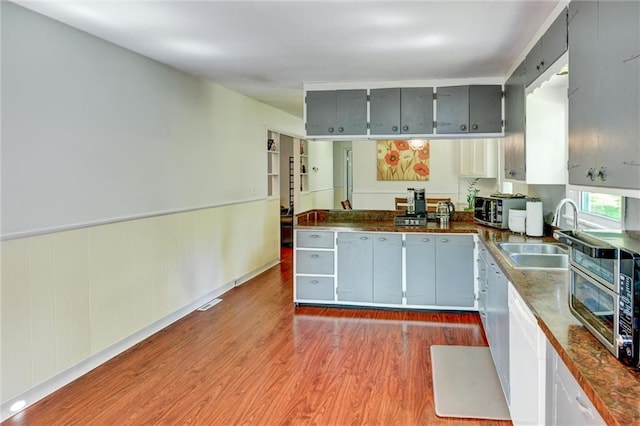 16128 Midland Dr, Shawnee, KS 66217 - kitchen with gray cabinets, dark countertops, wood finished floors, a peninsula, and a wainscoted wall