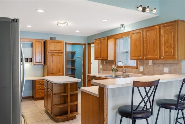 200 S Park Dr, Raymore, MO 64083 - kitchen with freestanding refrigerator, a peninsula, open shelves, brown cabinetry, and light tile patterned floors