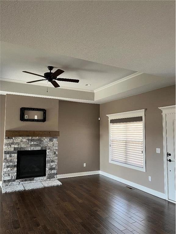 15653 Lakeside Dr, Basehor, KS 66007 - unfurnished living room featuring hardwood / wood-style floors, a raised ceiling, a stone fireplace, a ceiling fan, and crown molding