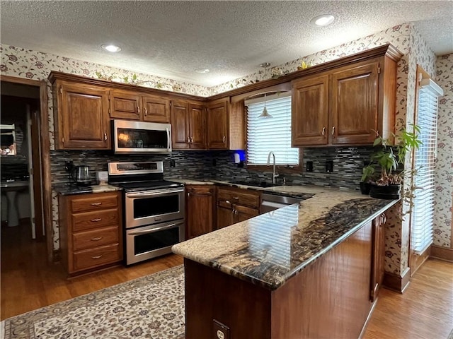 505 Williamsburg Dr, Lees Summit, MO 64063 - kitchen featuring appliances with stainless steel finishes, a textured ceiling, light wood finished floors, wallpapered walls, and a peninsula