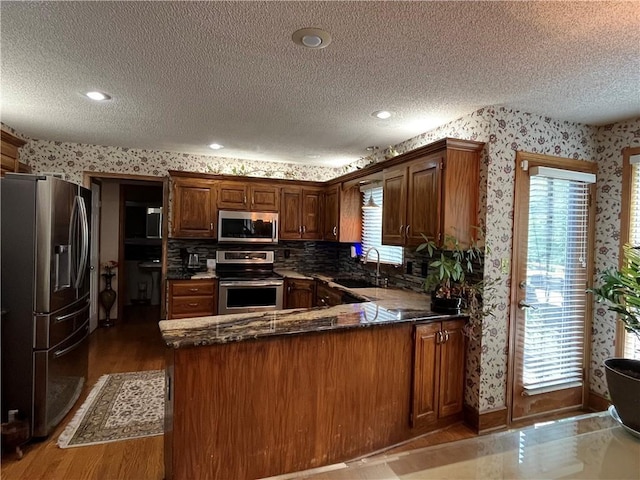 505 Williamsburg Dr, Lees Summit, MO 64063 - kitchen with stainless steel appliances, wallpapered walls, a textured ceiling, wood finished floors, and a peninsula