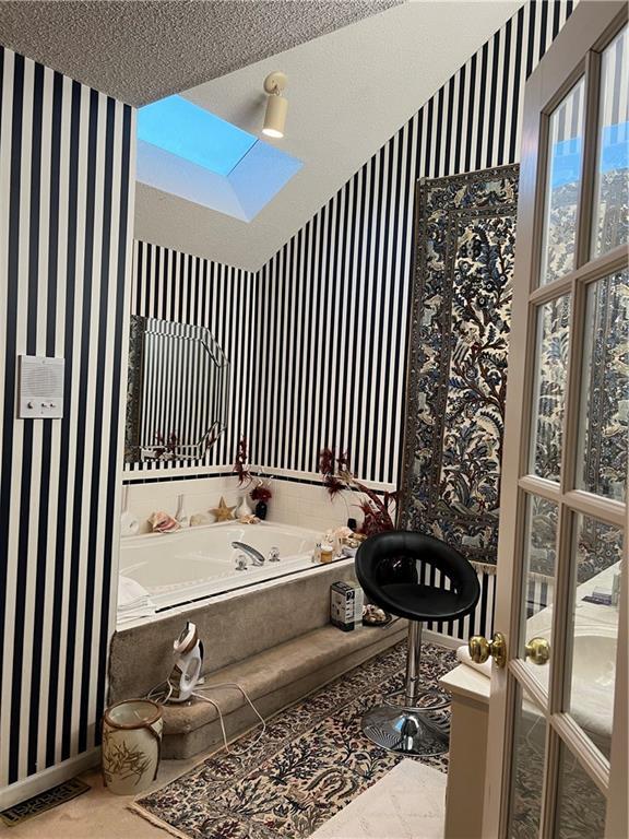 505 Williamsburg Dr, Lees Summit, MO 64063 - bathroom with wallpapered walls, a skylight, a garden tub, and a textured ceiling