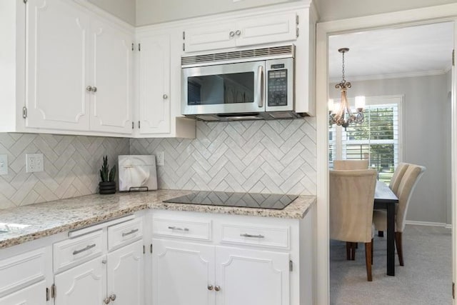 5501 W 86th St, Overland Park, KS 66207 - kitchen featuring stainless steel microwave, black electric stovetop, a chandelier, white cabinets, and backsplash