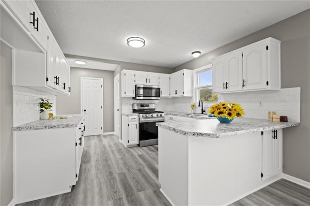 23404 Waverly Rd, Spring Hill, KS 66083 - kitchen featuring appliances with stainless steel finishes, a peninsula, light wood finished floors, white cabinets, and decorative backsplash