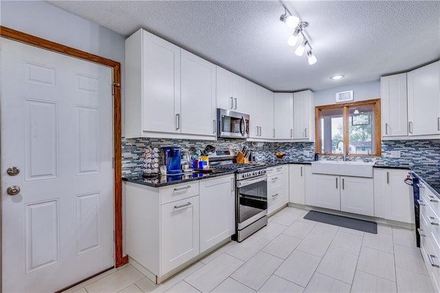 601 W 14th St, Pleasanton, KS 66075 - kitchen with stainless steel appliances, dark countertops, a textured ceiling, decorative backsplash, and white cabinets