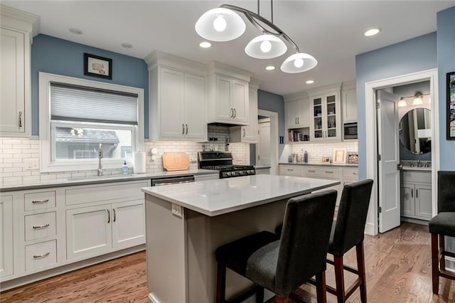 6033 Central St, Kansas City, MO 64113 - kitchen with appliances with stainless steel finishes, a kitchen bar, light wood-style floors, backsplash, and white cabinetry