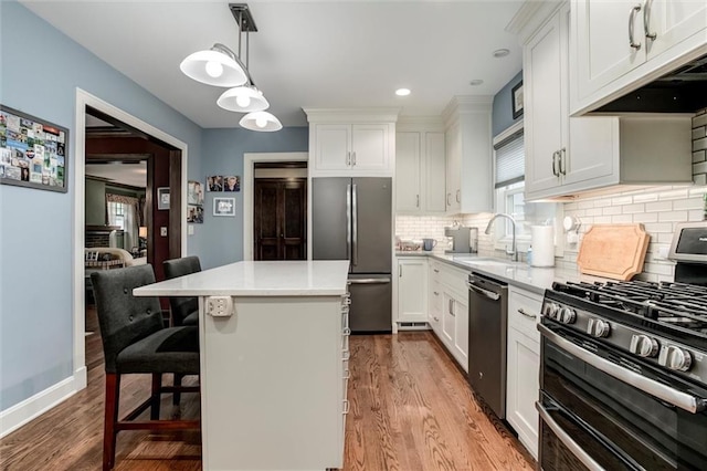 6033 Central St, Kansas City, MO 64113 - kitchen featuring appliances with stainless steel finishes, under cabinet range hood, wood finished floors, light countertops, and recessed lighting