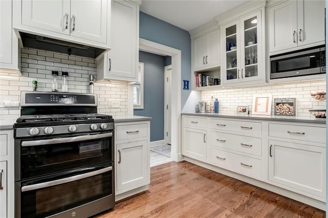 6033 Central St, Kansas City, MO 64113 - kitchen featuring appliances with stainless steel finishes, extractor fan, light countertops, tasteful backsplash, and white cabinets