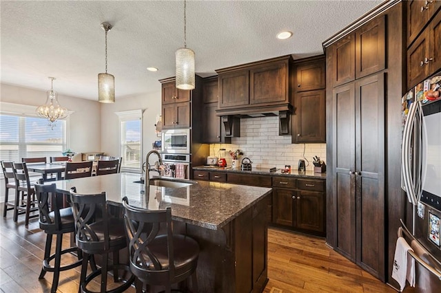 1401 Spurlock Cv, Raymore, MO 64083 - kitchen featuring appliances with stainless steel finishes, dark wood finished floors, decorative backsplash, a textured ceiling, and a breakfast bar