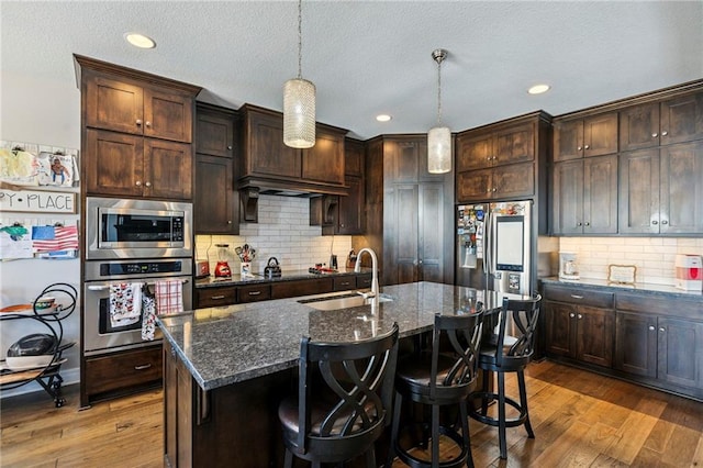 1401 Spurlock Cv, Raymore, MO 64083 - kitchen with appliances with stainless steel finishes, hardwood / wood-style floors, decorative backsplash, dark stone countertops, and a textured ceiling