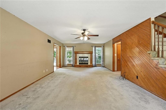 802 S Morgan Dr, Peculiar, MO 64078 - unfurnished living room featuring a tiled fireplace, stairs, ceiling fan, wood walls, and light colored carpet