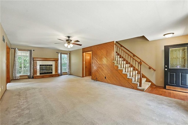802 S Morgan Dr, Peculiar, MO 64078 - unfurnished living room with stairs, wood walls, carpet flooring, a fireplace, and a ceiling fan