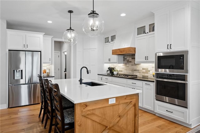 9260 Saddletop St, Lenexa, KS 66227 - kitchen with stainless steel appliances, light wood-style floors, glass insert cabinets, a center island with sink, and recessed lighting