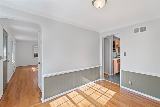 7712 Mcgee St, Kansas City, MO 64114 - spare room with arched walkways, light wood-style flooring, wainscoting, and ornamental molding