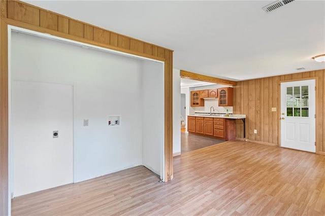 7712 Mcgee St, Kansas City, MO 64114 - kitchen featuring light countertops, light wood-type flooring, brown cabinets, wood walls, and glass insert cabinets