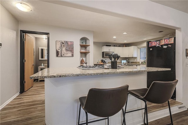 792 195th St, Fort Scott, KS 66701 - kitchen with stainless steel microwave, white cabinetry, light wood finished floors, a breakfast bar area, and light stone counters