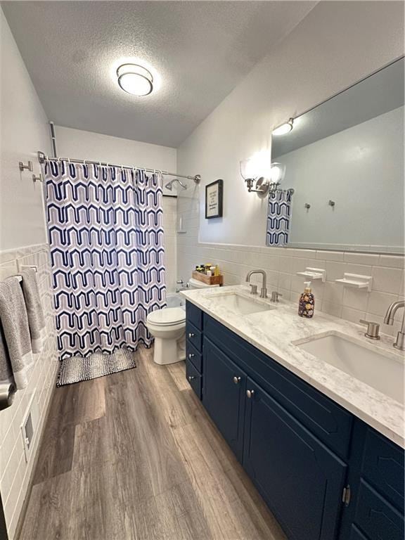 12913 E 41st St S, Independence, MO 64055 - bathroom featuring tile walls, a textured ceiling, double vanity, wood finished floors, and wainscoting