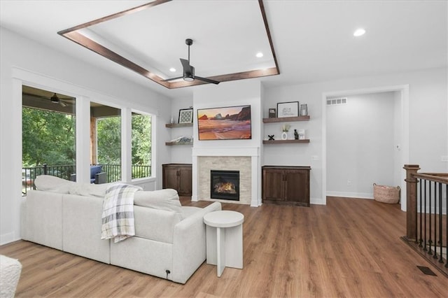 1161 SW Whitby Dr, Lees Summit, MO 64083 - living area featuring a ceiling fan, a glass covered fireplace, a tray ceiling, light wood-type flooring, and recessed lighting