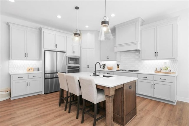 1161 SW Whitby Dr, Lees Summit, MO 64083 - kitchen featuring stainless steel appliances, decorative backsplash, light wood-style flooring, a kitchen island with sink, and light countertops