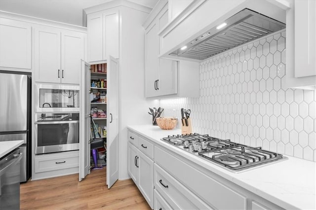 1161 SW Whitby Dr, Lees Summit, MO 64083 - kitchen with appliances with stainless steel finishes, custom exhaust hood, white cabinets, decorative backsplash, and light wood-type flooring