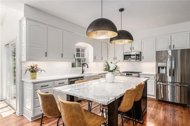11401 Cedar St, Leawood, KS 66211 - kitchen featuring appliances with stainless steel finishes, light wood-style floors, backsplash, light stone counters, and a center island