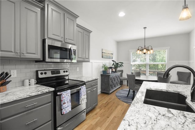 1013 SE Beatty Ct, Blue Springs, MO 64014 - kitchen with appliances with stainless steel finishes, gray cabinets, a chandelier, light wood-type flooring, and decorative backsplash