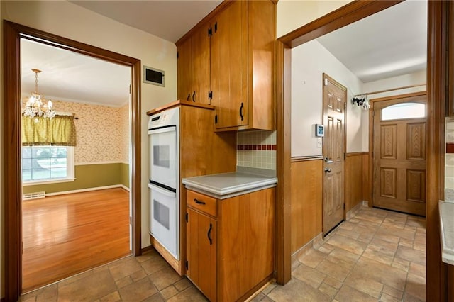 4411 W 89th St, Prairie Village, KS 66207 - kitchen featuring a chandelier, stone tile flooring, white double oven, light countertops, and a wainscoted wall