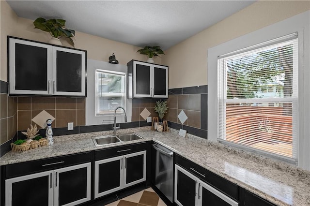 3230 Bellefontaine Ave, Kansas City, MO 64128 - kitchen featuring dark cabinetry, stainless steel dishwasher, glass insert cabinets, light stone countertops, and backsplash