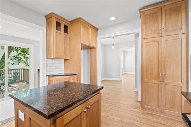 1535 W 75th St, Kansas City, MO 64114 - kitchen featuring light wood finished floors, glass insert cabinets, backsplash, dark stone countertops, and a kitchen island
