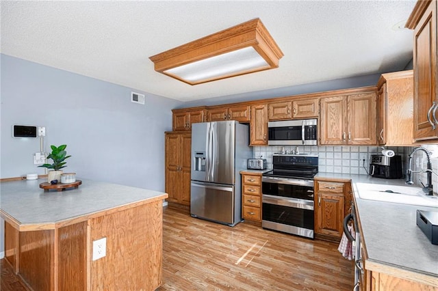 2417 SW Woodhaven Ln, Lees Summit, MO 64082 - kitchen with stainless steel appliances, light wood-style flooring, backsplash, light countertops, and a textured ceiling