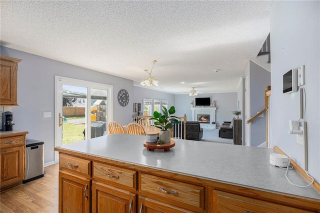 2417 SW Woodhaven Ln, Lees Summit, MO 64082 - kitchen featuring brown cabinets, a textured ceiling, a lit fireplace, a chandelier, and light wood finished floors