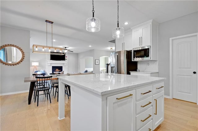 20487 W 108th St, Olathe, KS 66061 - kitchen featuring stainless steel appliances, a lit fireplace, light wood-style floors, open floor plan, and a kitchen island