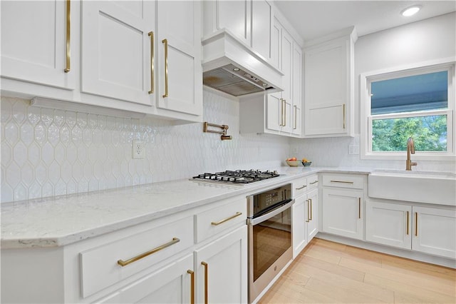 20487 W 108th St, Olathe, KS 66061 - kitchen with appliances with stainless steel finishes, custom exhaust hood, white cabinetry, light wood-type flooring, and tasteful backsplash