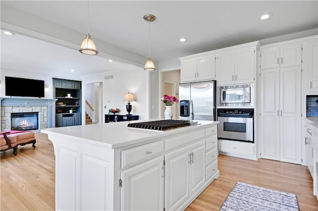 5010 W 161st Ter, Overland Park, KS 66085 - kitchen featuring appliances with stainless steel finishes, a stone fireplace, light wood-style flooring, a center island, and light countertops