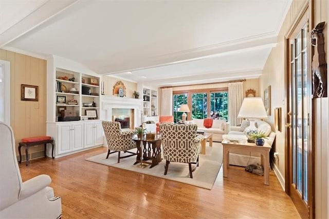 8422 Reinhardt Ln, Leawood, KS 66206 - living area featuring light wood-style floors, beam ceiling, a glass covered fireplace, crown molding, and built in shelves