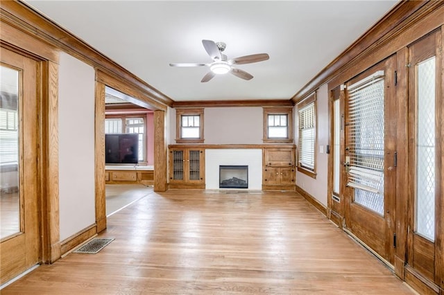 3509 Bellefontaine Ave, Kansas City, MO 64128 - unfurnished living room with ornamental molding, light wood-style flooring, a fireplace with flush hearth, ceiling fan, and healthy amount of natural light