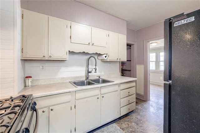 3509 Bellefontaine Ave, Kansas City, MO 64128 - kitchen with freestanding refrigerator, stainless steel gas range oven, white cabinetry, light countertops, and tasteful backsplash