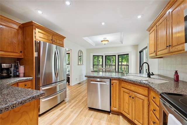 1311 SE Eastridge Cir, Blue Springs, MO 64014 - kitchen featuring stainless steel appliances, a raised ceiling, a peninsula, light wood-style floors, and brown cabinetry