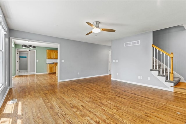 1321 SW Crossing Dr, Lees Summit, MO 64081 - unfurnished living room with ceiling fan, light wood-type flooring, stairway, and a chandelier