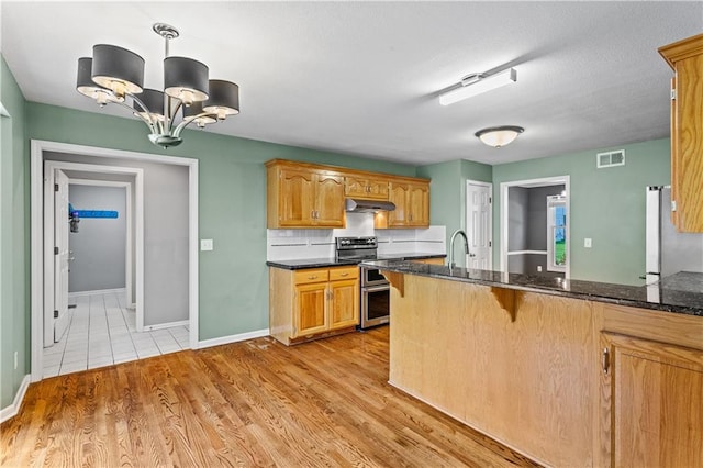 1321 SW Crossing Dr, Lees Summit, MO 64081 - kitchen with range with two ovens, a breakfast bar area, under cabinet range hood, a chandelier, and dark stone countertops